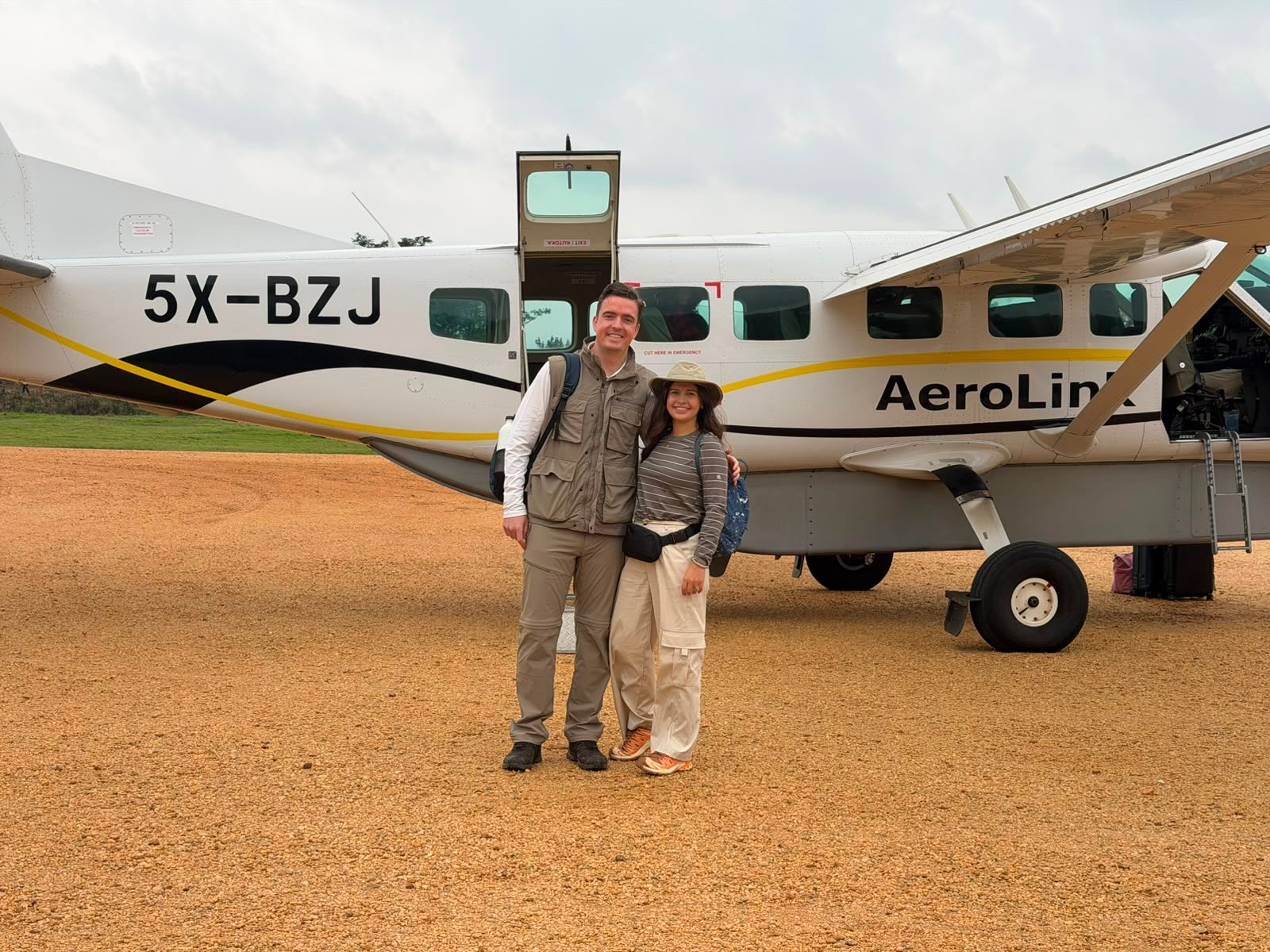 Two travellers standing in front of a small plane on an airstrip in Uganda