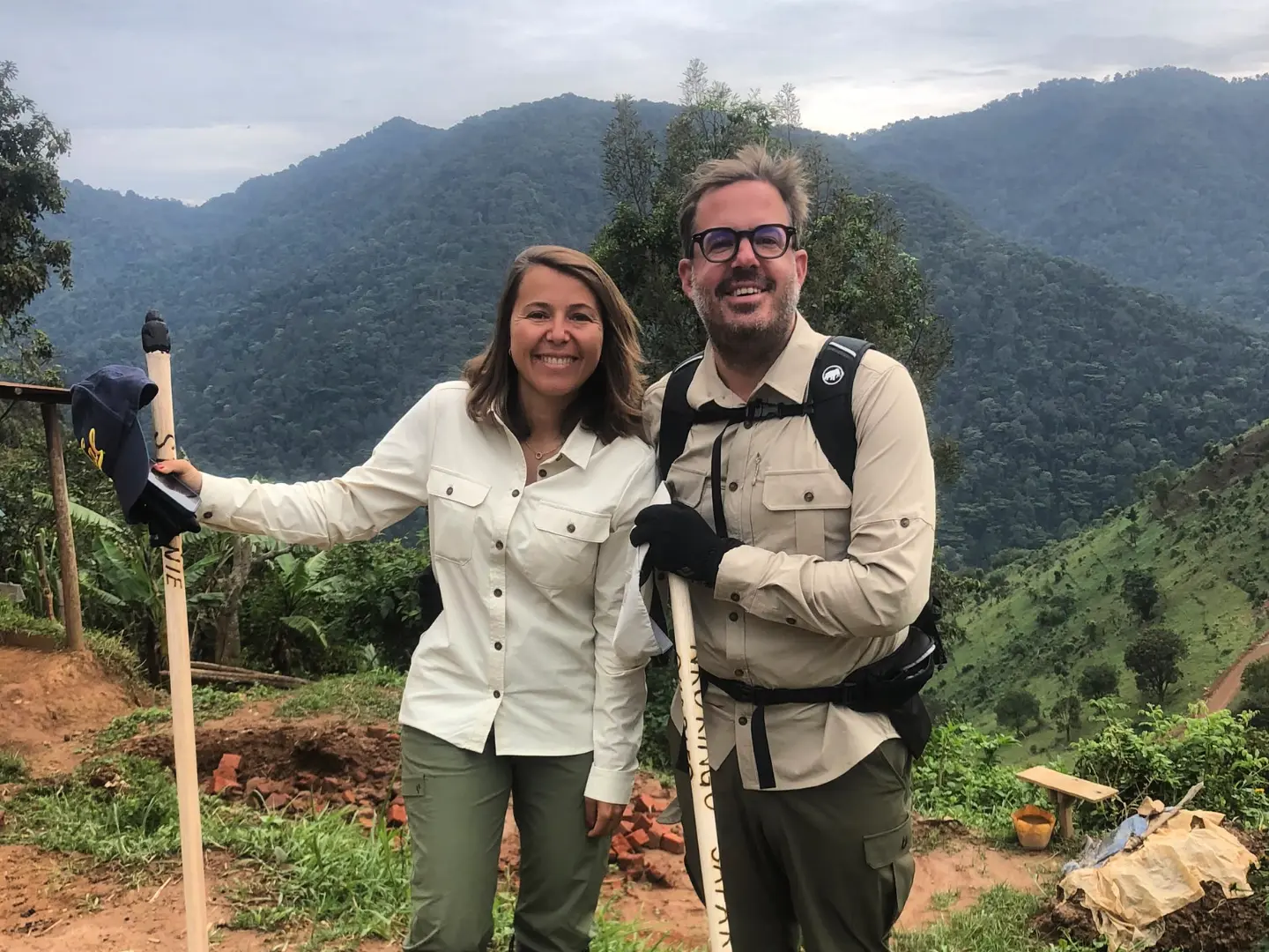 A couple with walking sticks standing against green mountains in Uganda