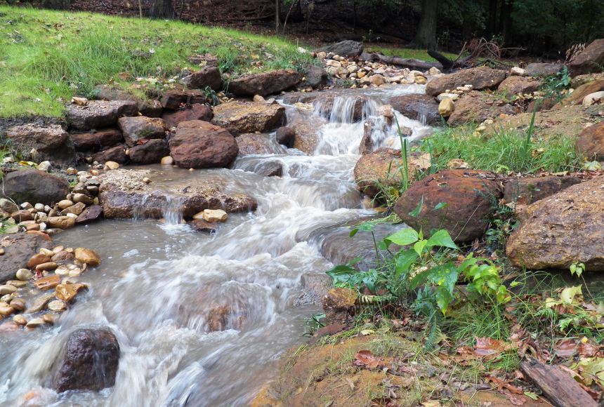 Image of a stream running over rocks in a neighborhood.