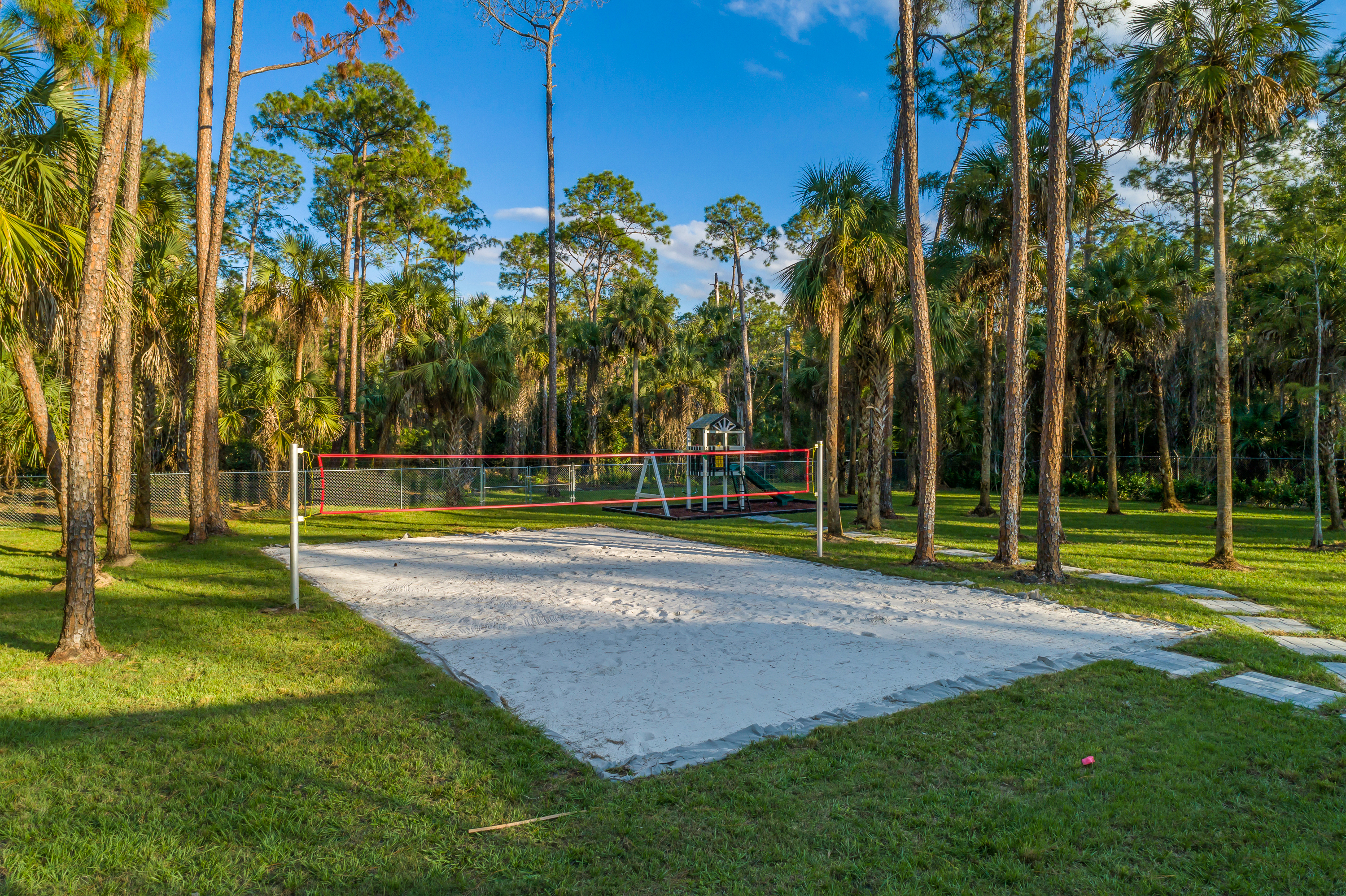 Outdoor sand volleyball court with net surrounded by tall trees and grass