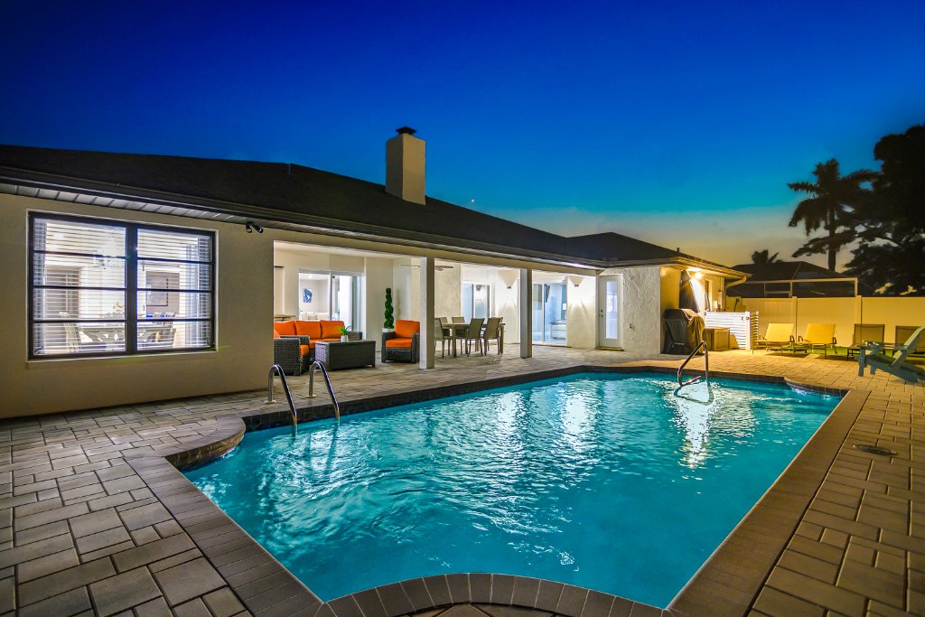 Swimming pool and lit patio area with orange outdoor seating and dining table at dusk