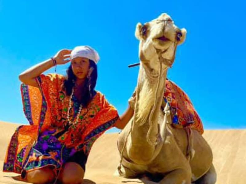 Visitor beside a resting camel on the dunes near Essaouira