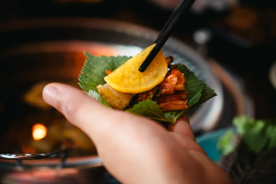 A hand holding a small lettuce wrap with grilled meat