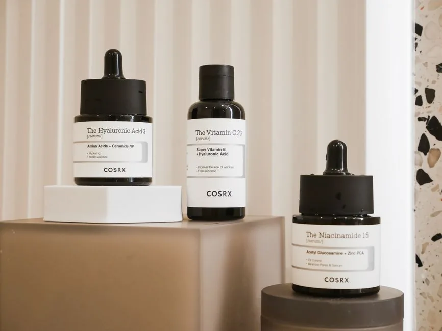A minimal arrangement of Korean skincare products — a serum, essence, and moisturizer — on a neutral surface