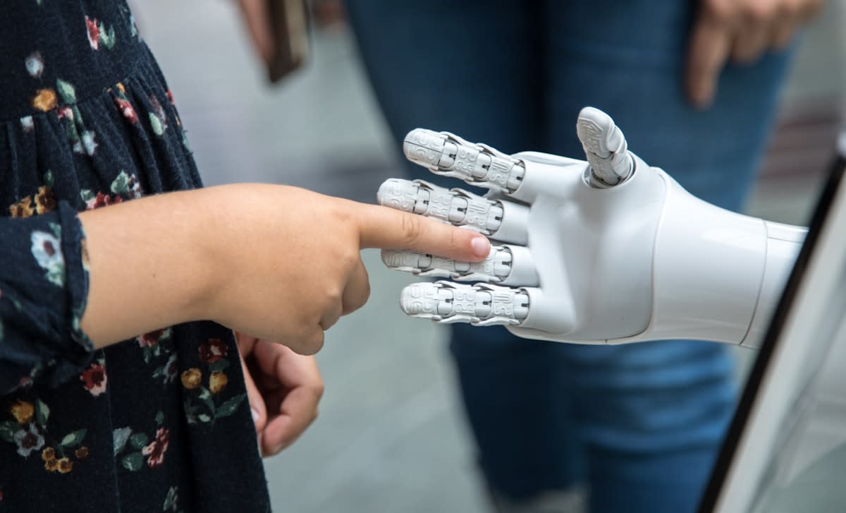 Close up of a human hand and a robotic hand collaborating on a blueprint