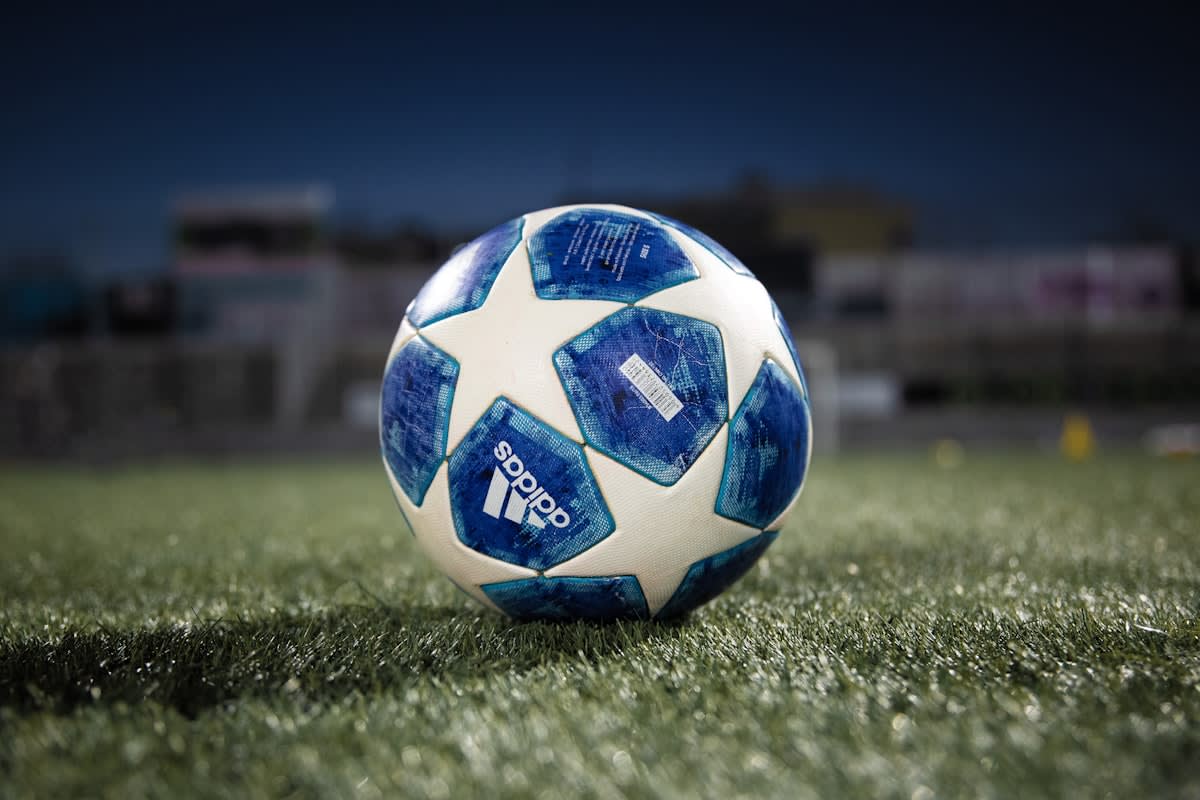 Close up of a soccer ball on grass with a blur of a stadium in the background