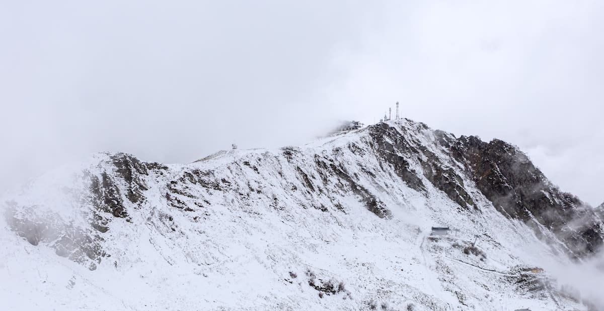 A lone figure standing on a stark, white mountain peak under a grey sky