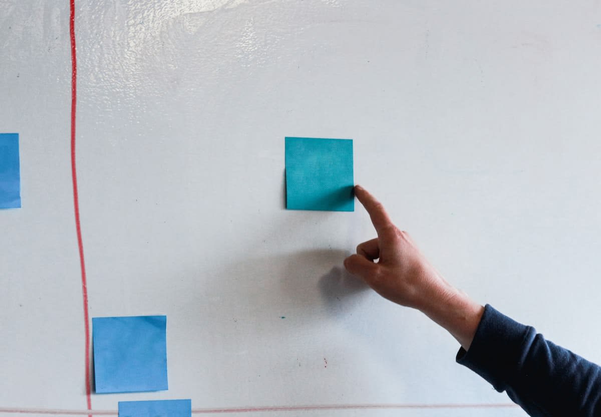 A close-up of a hand moving a sticky note on a glass wall with connecting lines