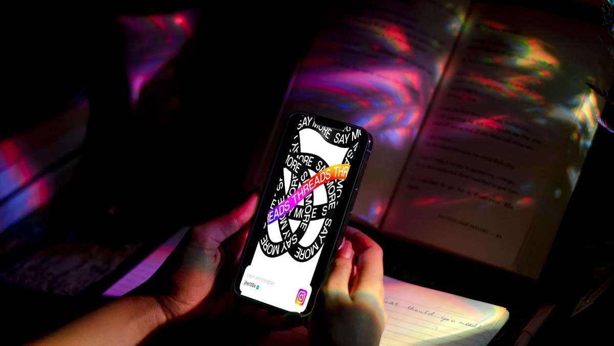 A person reading a physical book next to a glowing smartphone