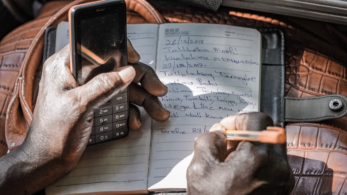 A person meticulously writing in a ledger with a calculator nearby