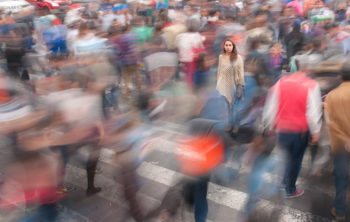 A crowded city street with blurred people and one sharp, still figure