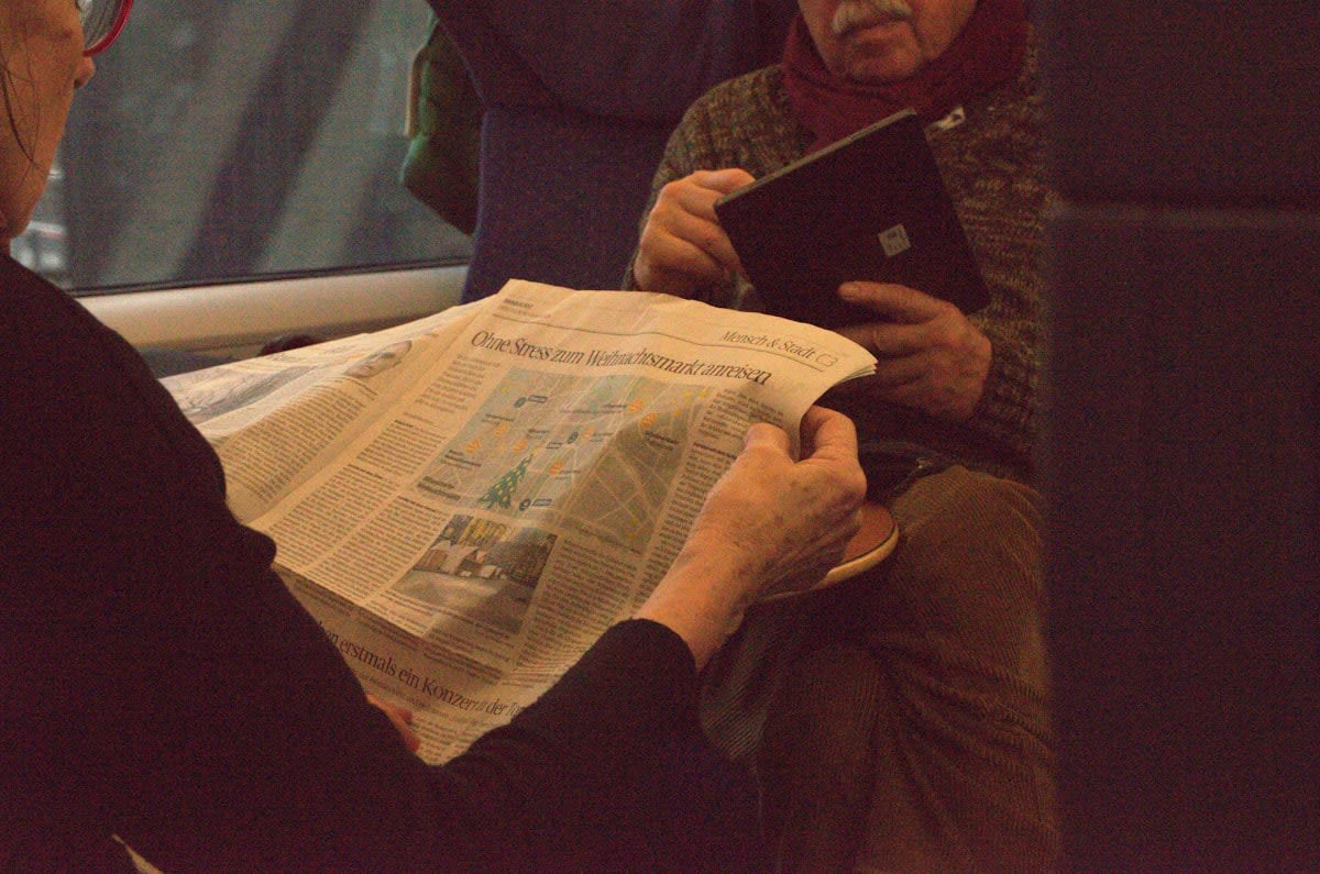 A person reading multiple physical newspapers and a digital tablet