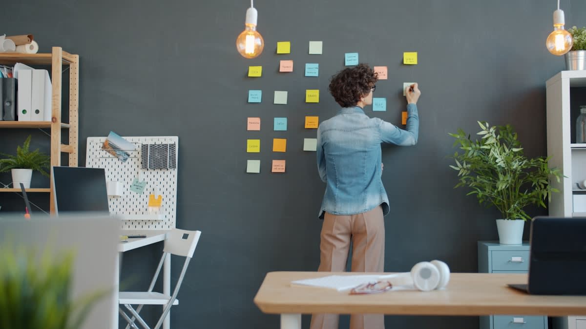 Person writing on a large glass whiteboard in a modern office