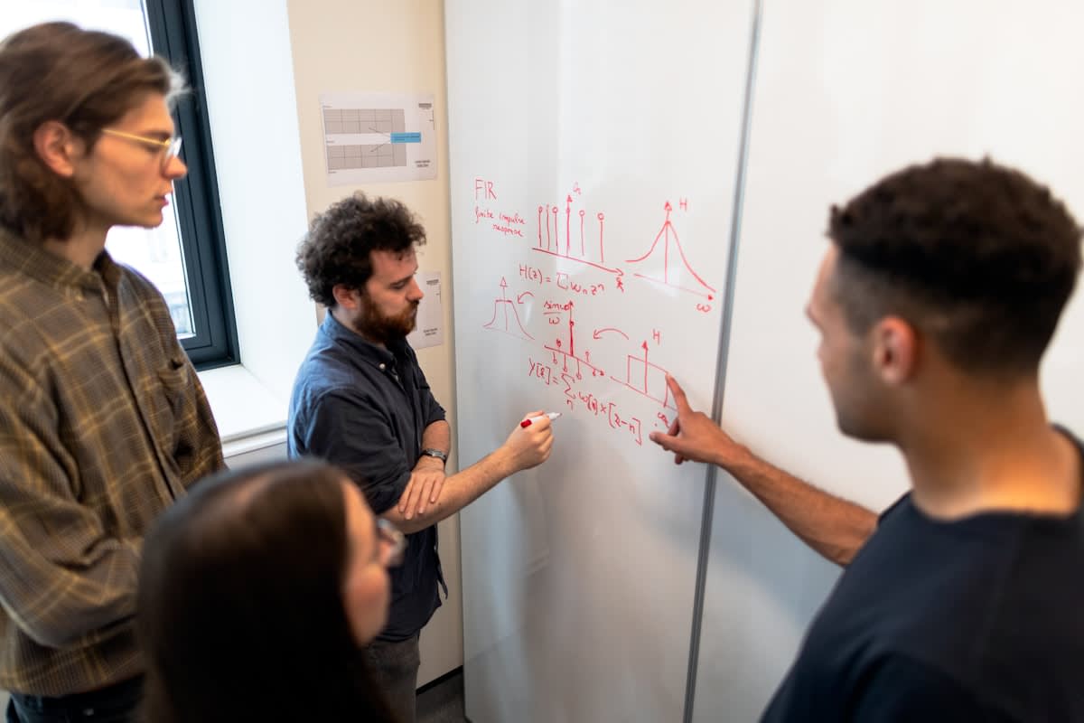 People collaborating around a whiteboard with complex diagrams