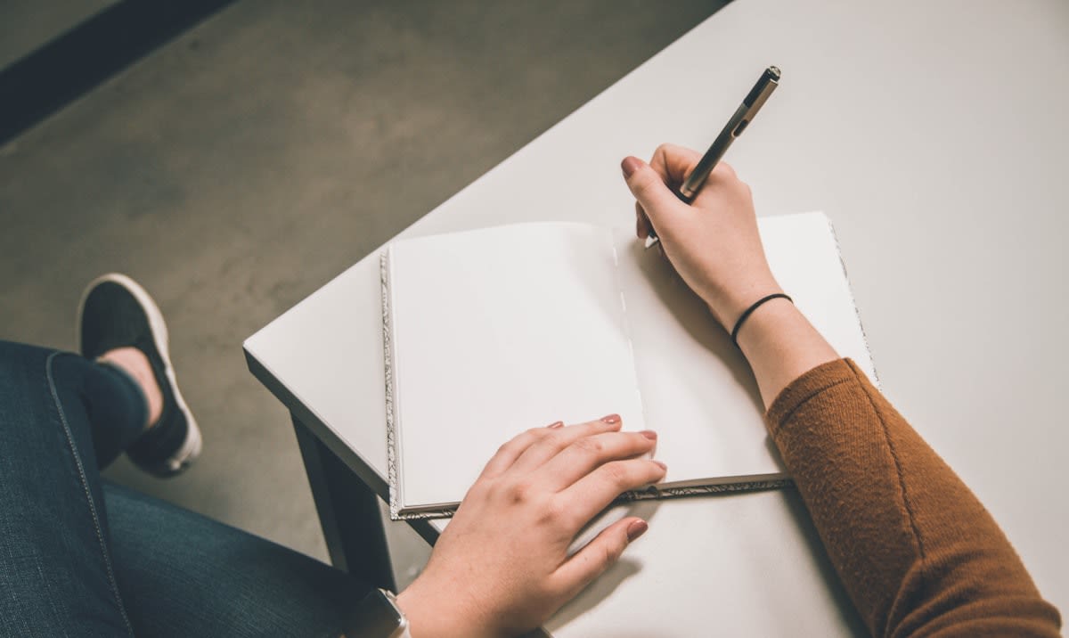 Person writing in a notebook next to a smartphone turned face down
