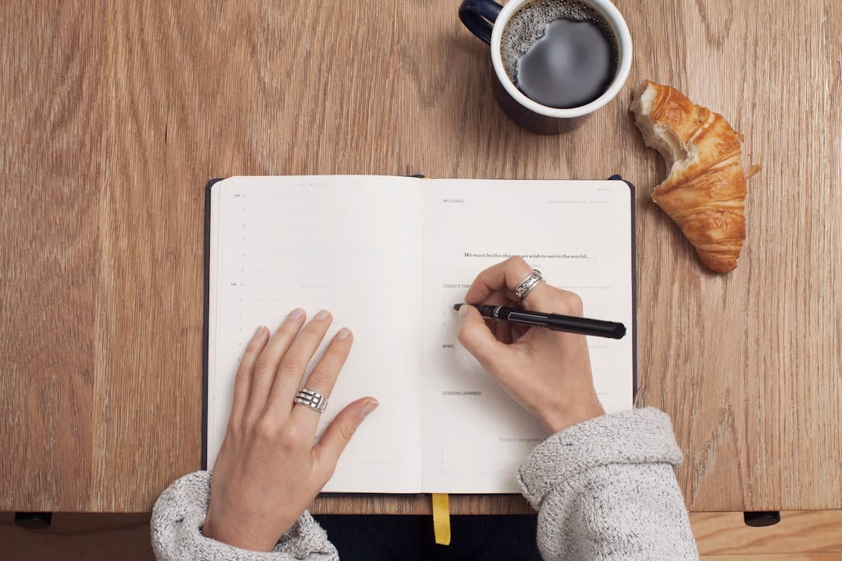 A person writing in a journal with a timer nearby
