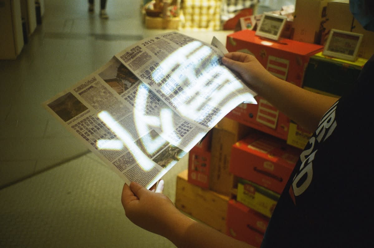 A person reading a physical newspaper next to a glowing smartphone