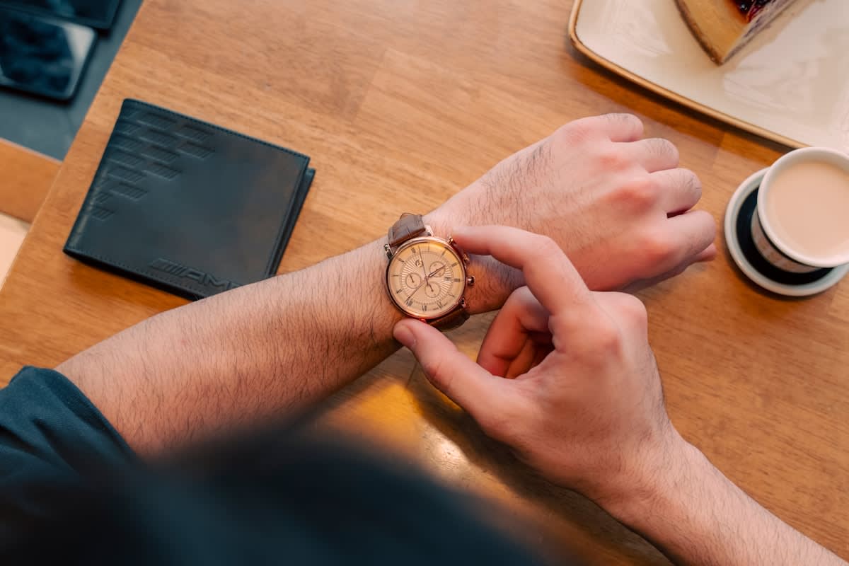 Close up of a watch and a coffee cup on a wooden table