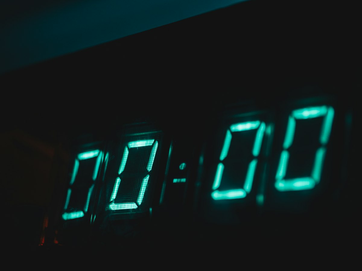 Close up of a digital clock showing 1:00 PM in a dim office