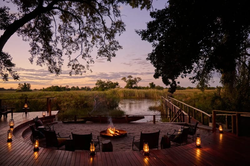 Outdoor fire deck at Nxamaseri Island Lodge with a central fire pit and chairs overlooking the river at sunset