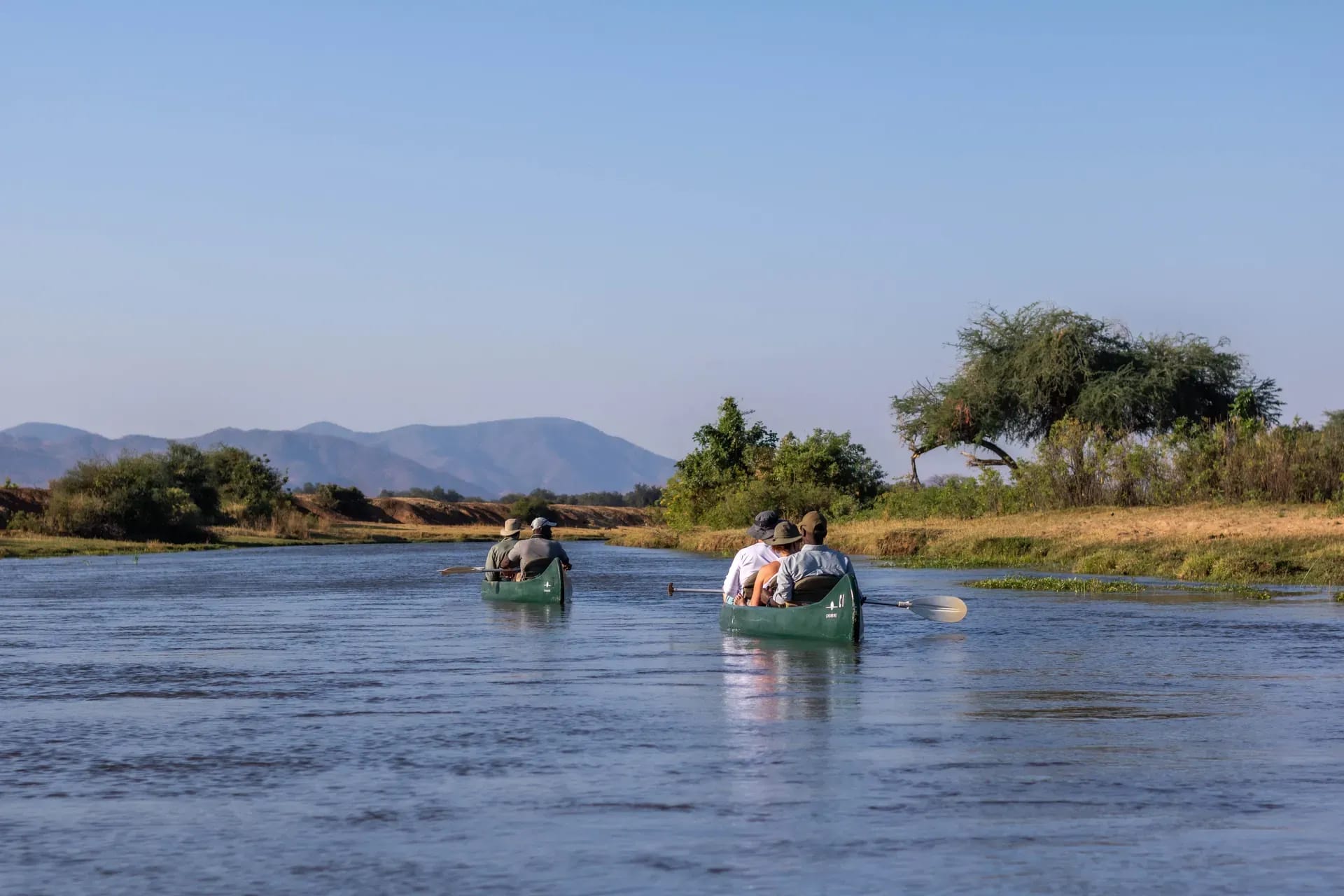 Boat carrying safari guests on a river during a water-based safari, with trees and hills in the background