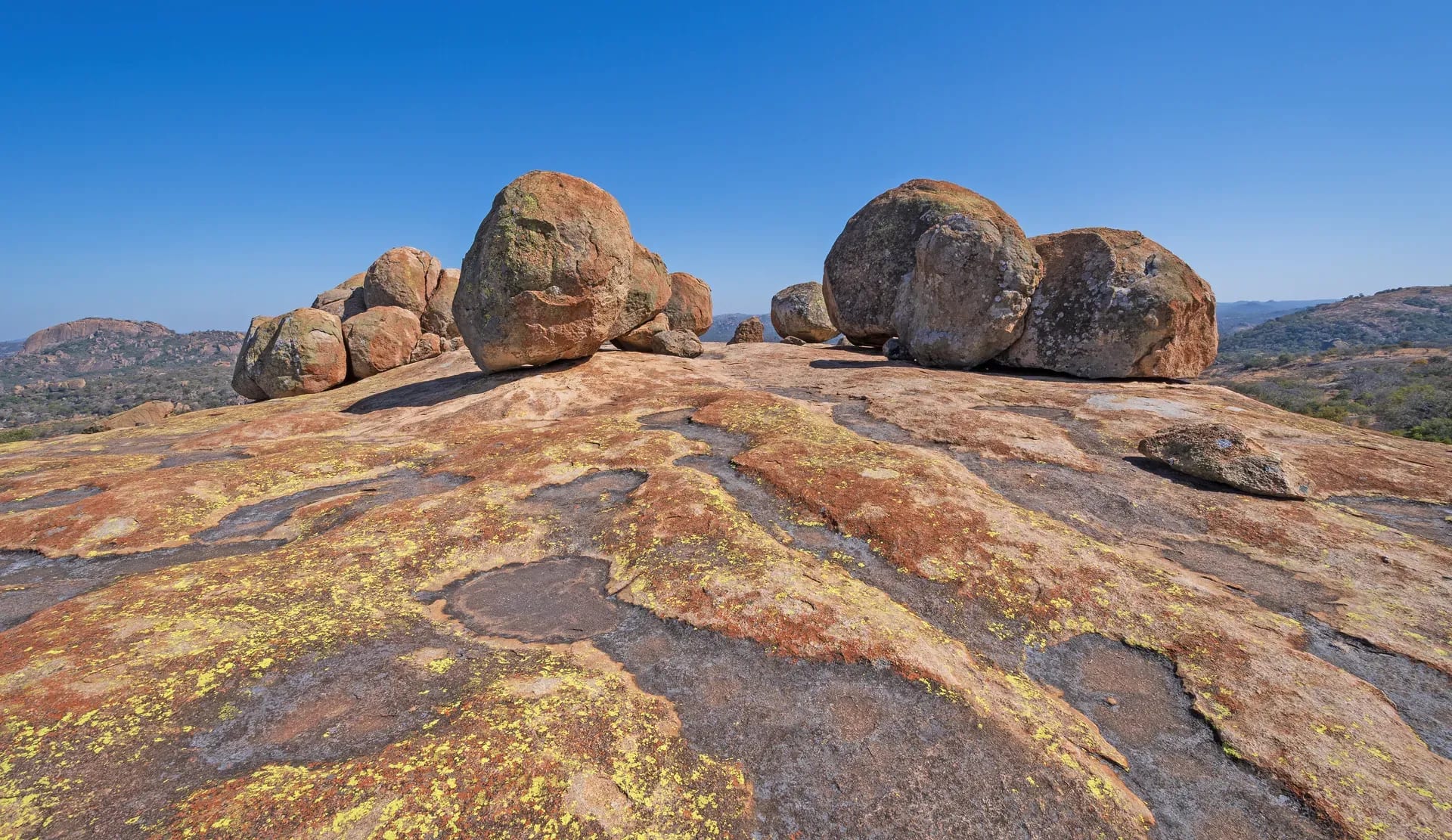 Distinctive granite rock formations in Matobo Hills rising above a golden grassy landscape under a clear blue sky