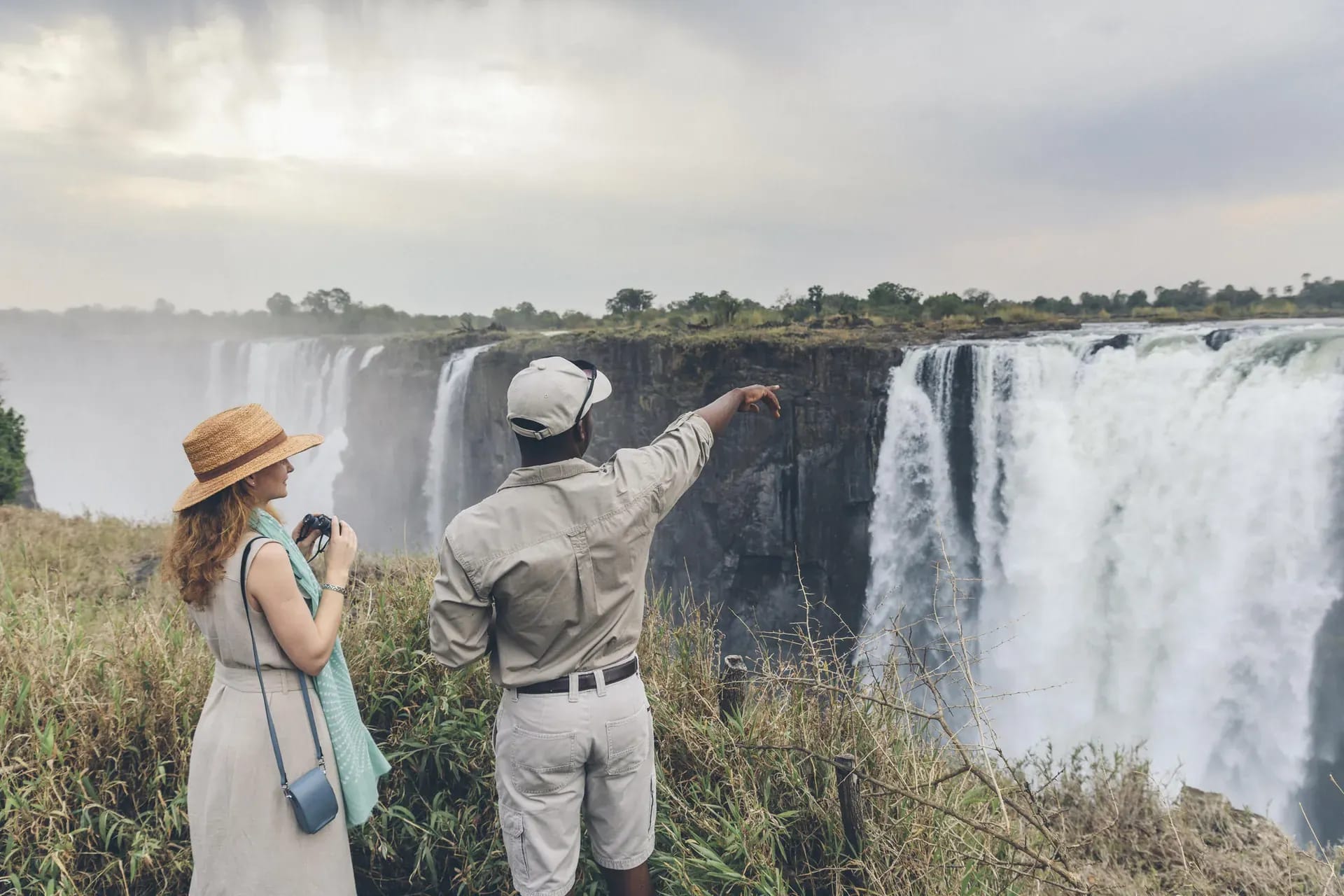 Tourist standing at a scenic viewpoint overlooking Victoria Falls with cascading water and lush cliffs
