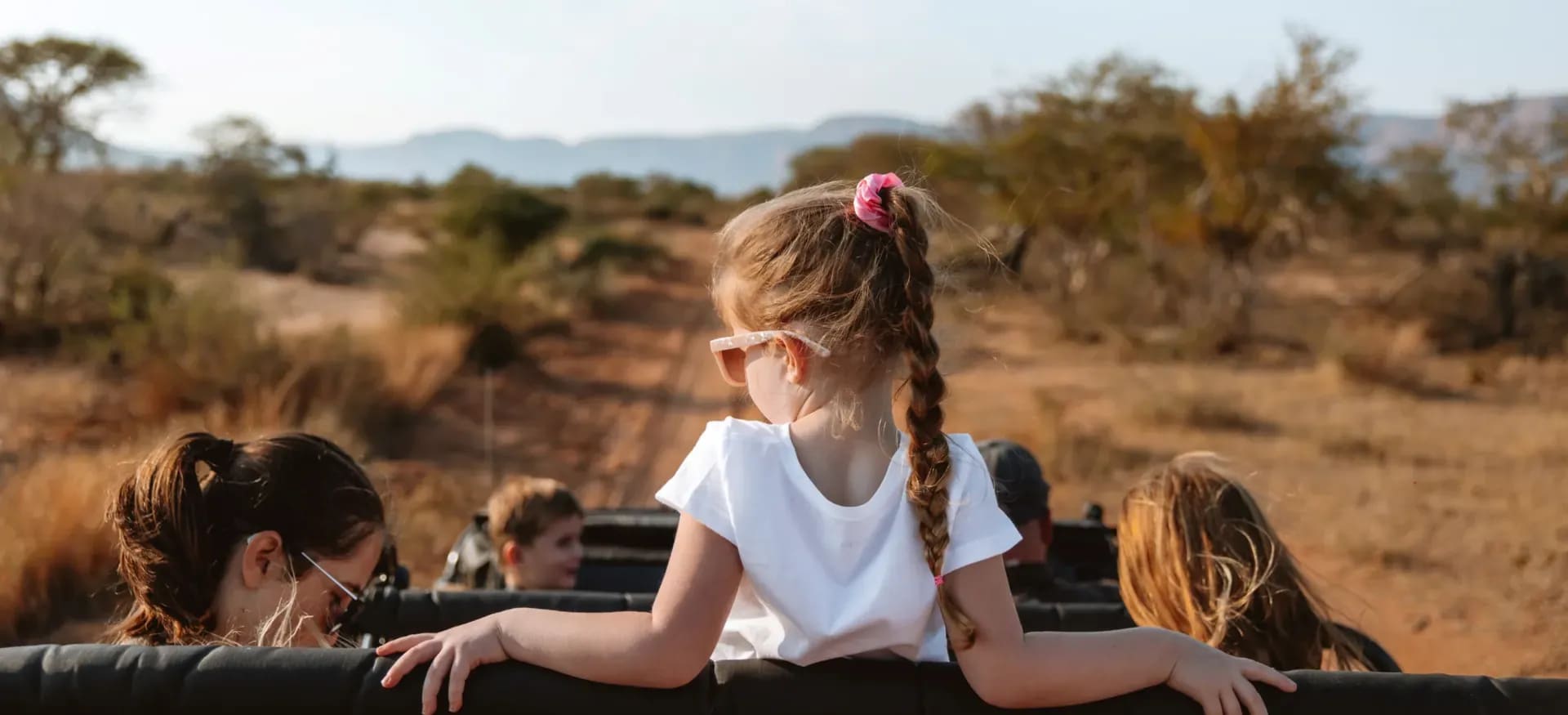 Young girl on safari wearing a hat, sitting in an open-air vehicle and enjoying the adventure