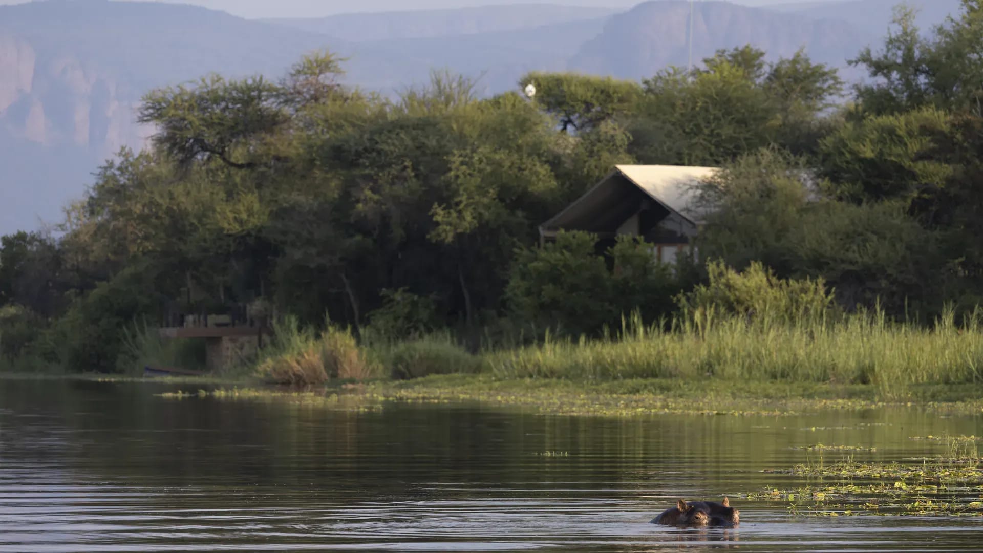View of a thatched-roof Marataba residence from a boat on the water surrounded by lush greenery