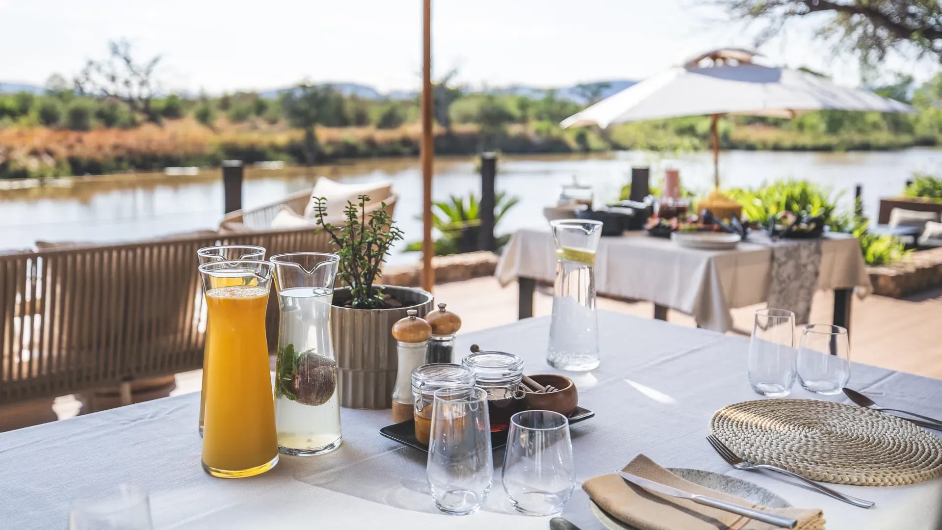 Breakfast table set up on an outdoor deck overlooking the landscape with white tablecloth and chairs