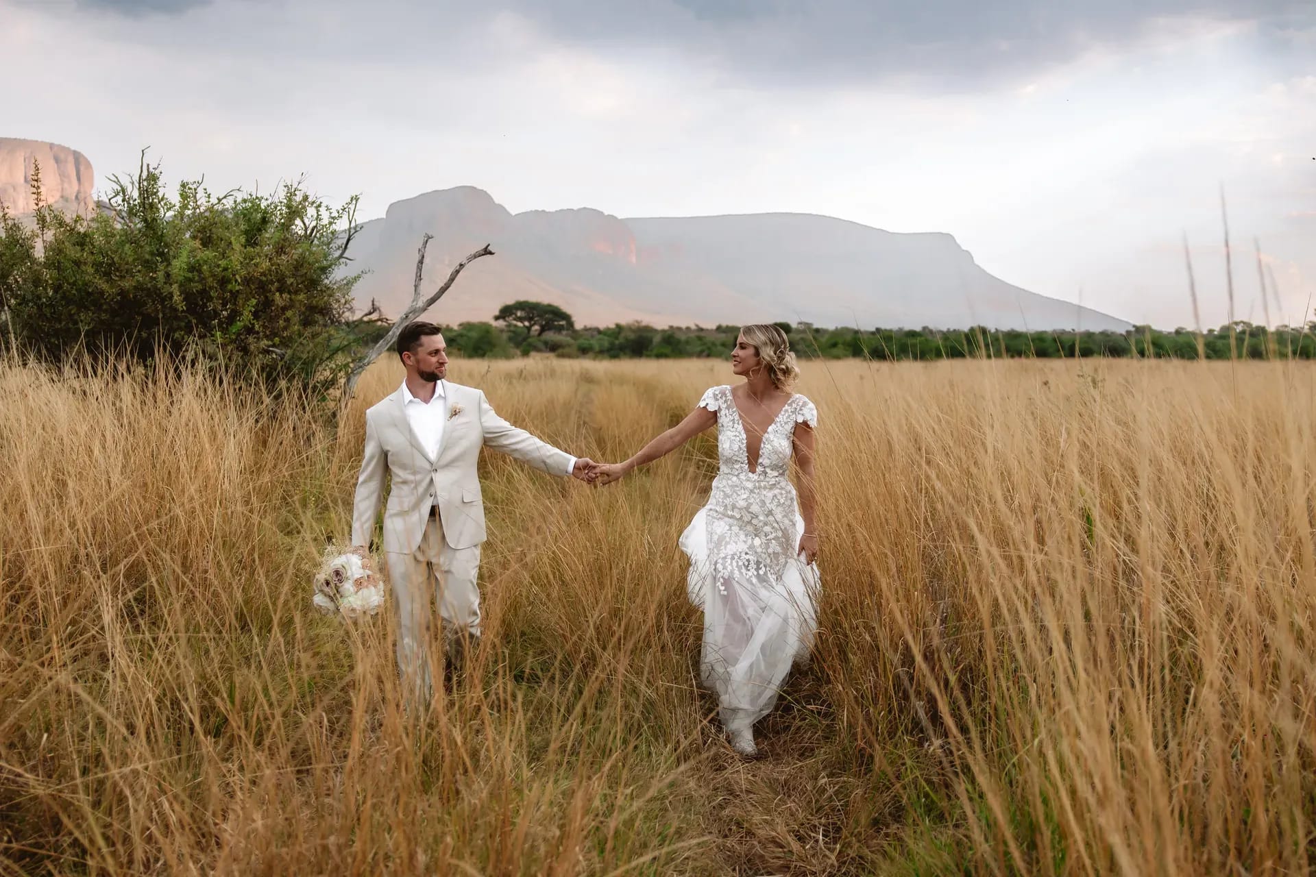 Just-married couple walking through the grass in the bush at Marataba with stunning surrounding views.