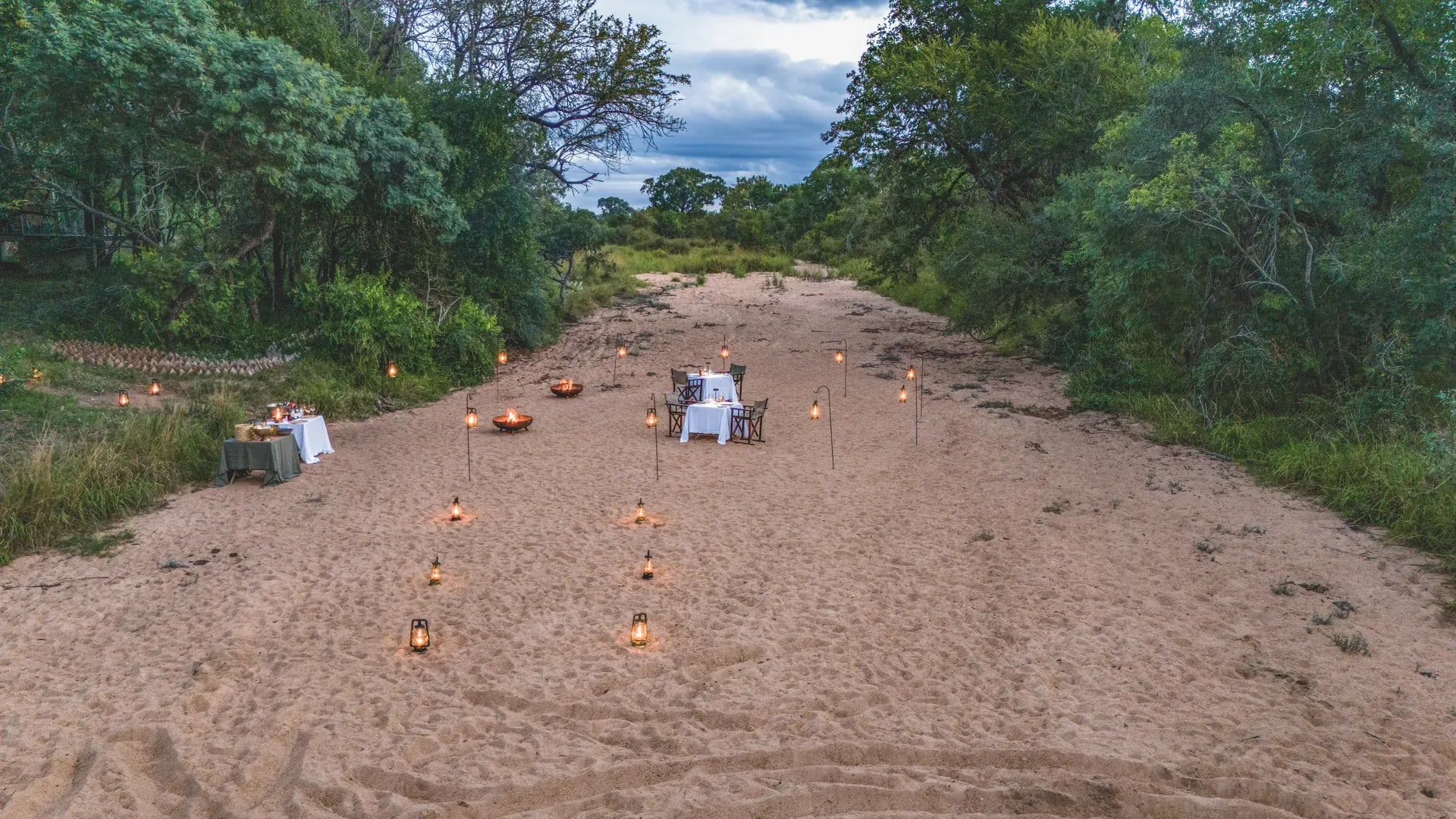 Romantic riverbed dining setup at Monwana Lodge, with a central table surrounded by candles and the natural African bush setting.