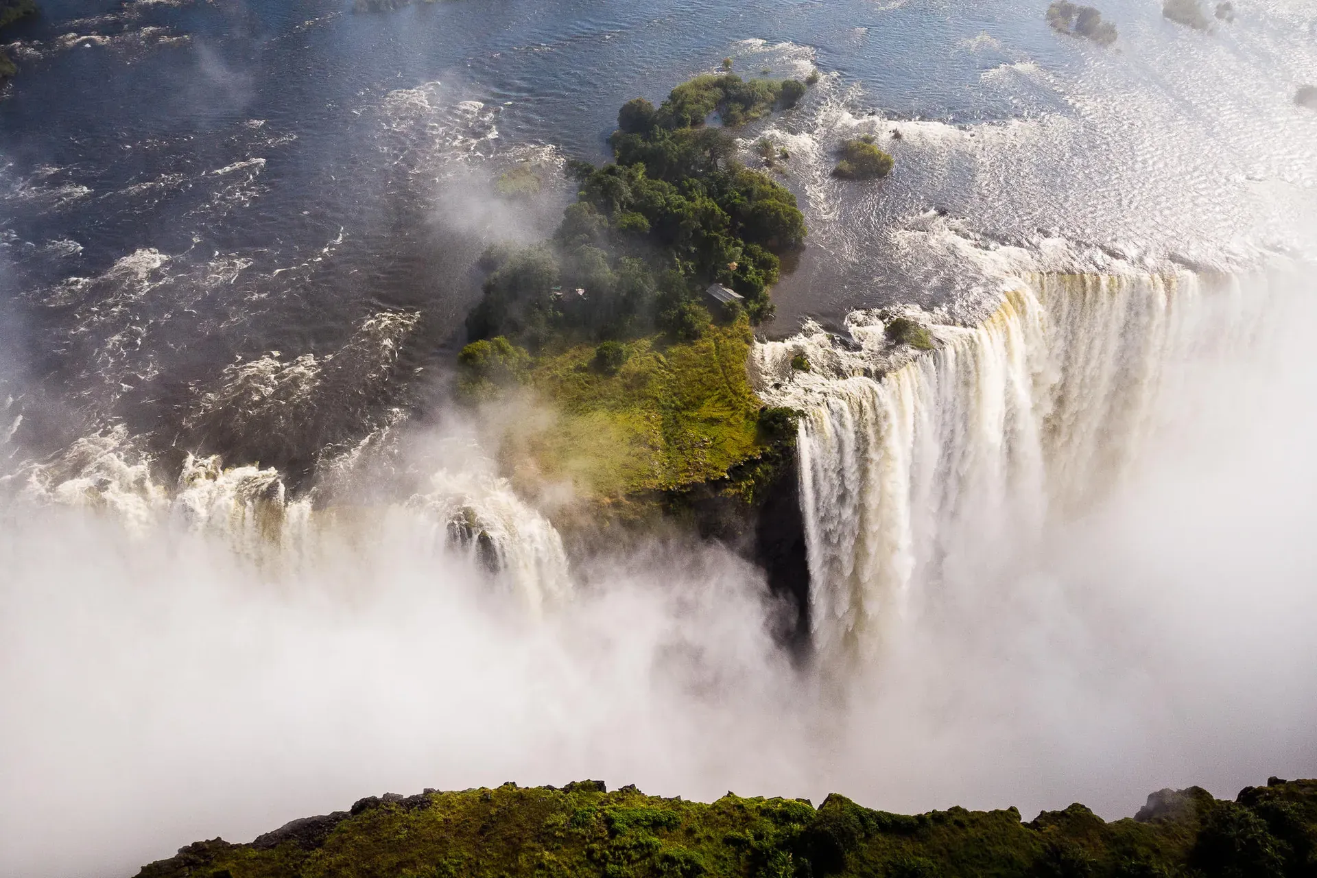 Helicopter flying above a dramatic waterfall with mist and lush green scenery
