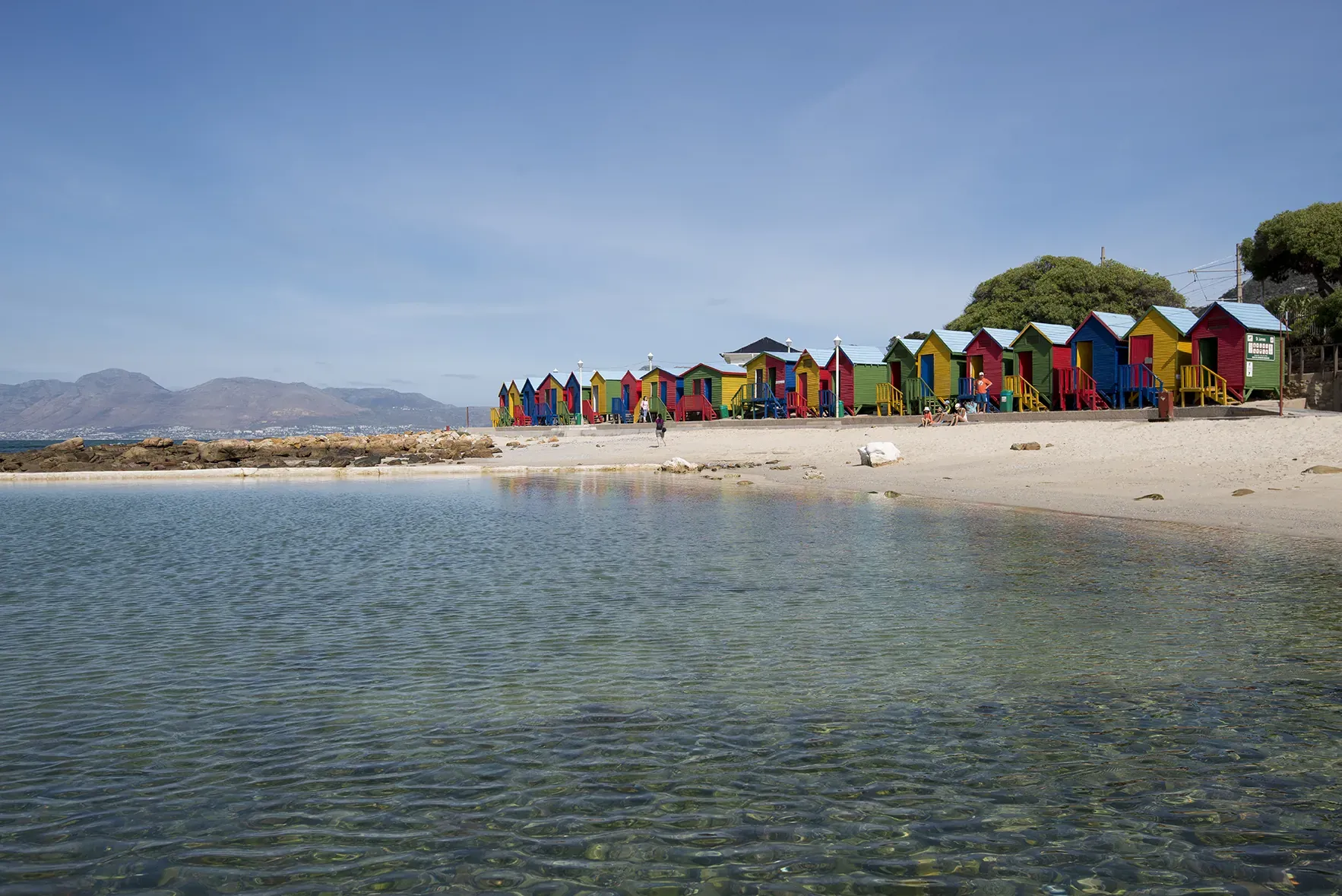 Row of colorful beach huts along St. James beach beside the ocean water