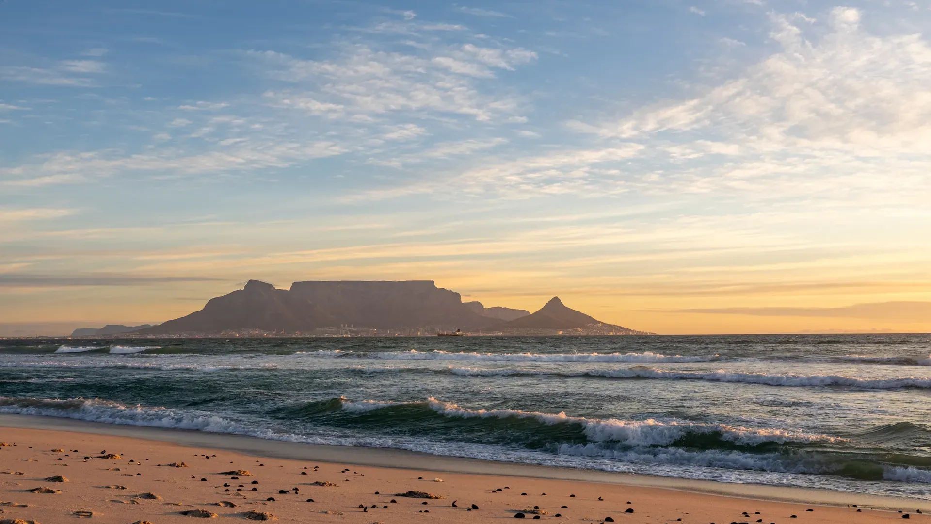 Sunset view of Cape Town's Table Mountain and Lion's Head with an orange sky and calm ocean water