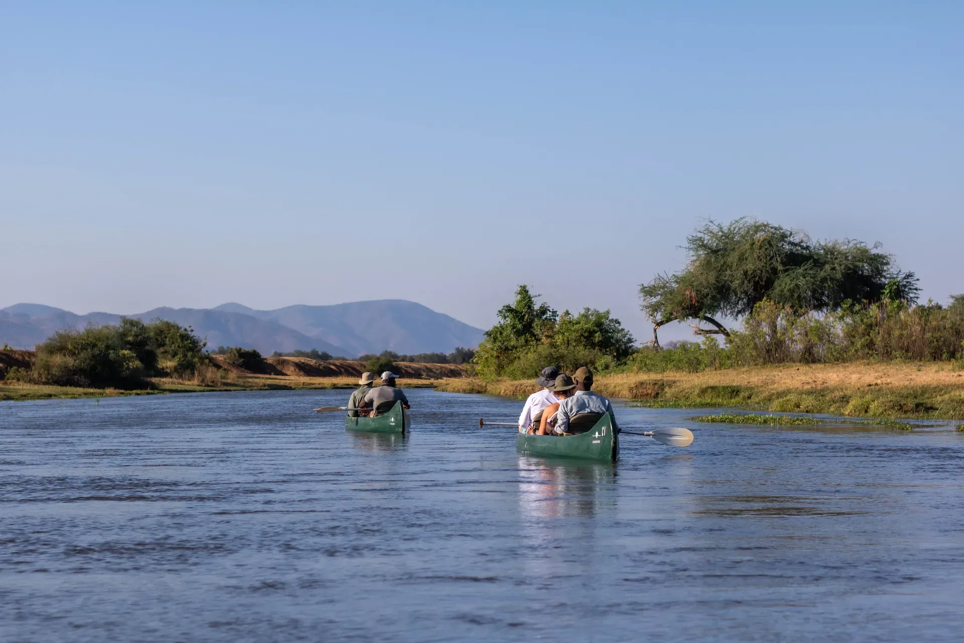 Boat carrying safari guests on a river during a water-based safari, with trees and hills in the background
