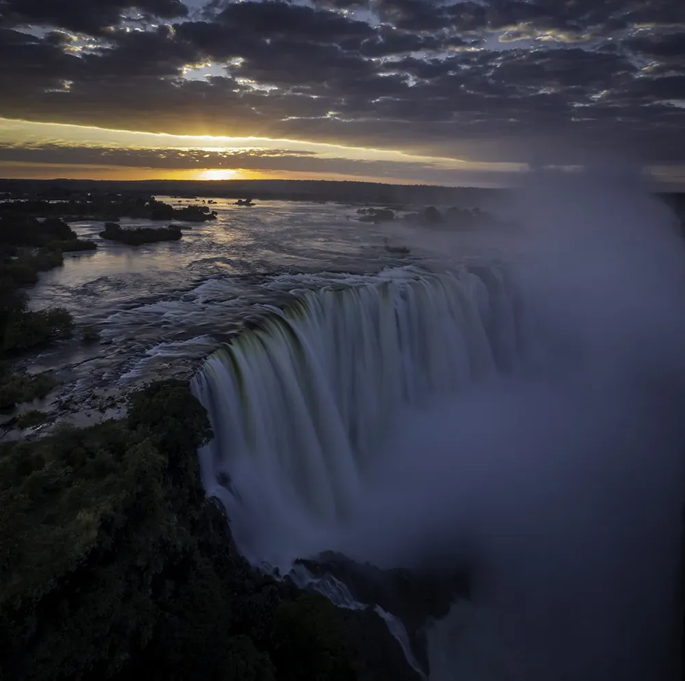 Majestic Victoria Falls cascading into a gorge with mist rising and dramatic clouds overhead during an adventure