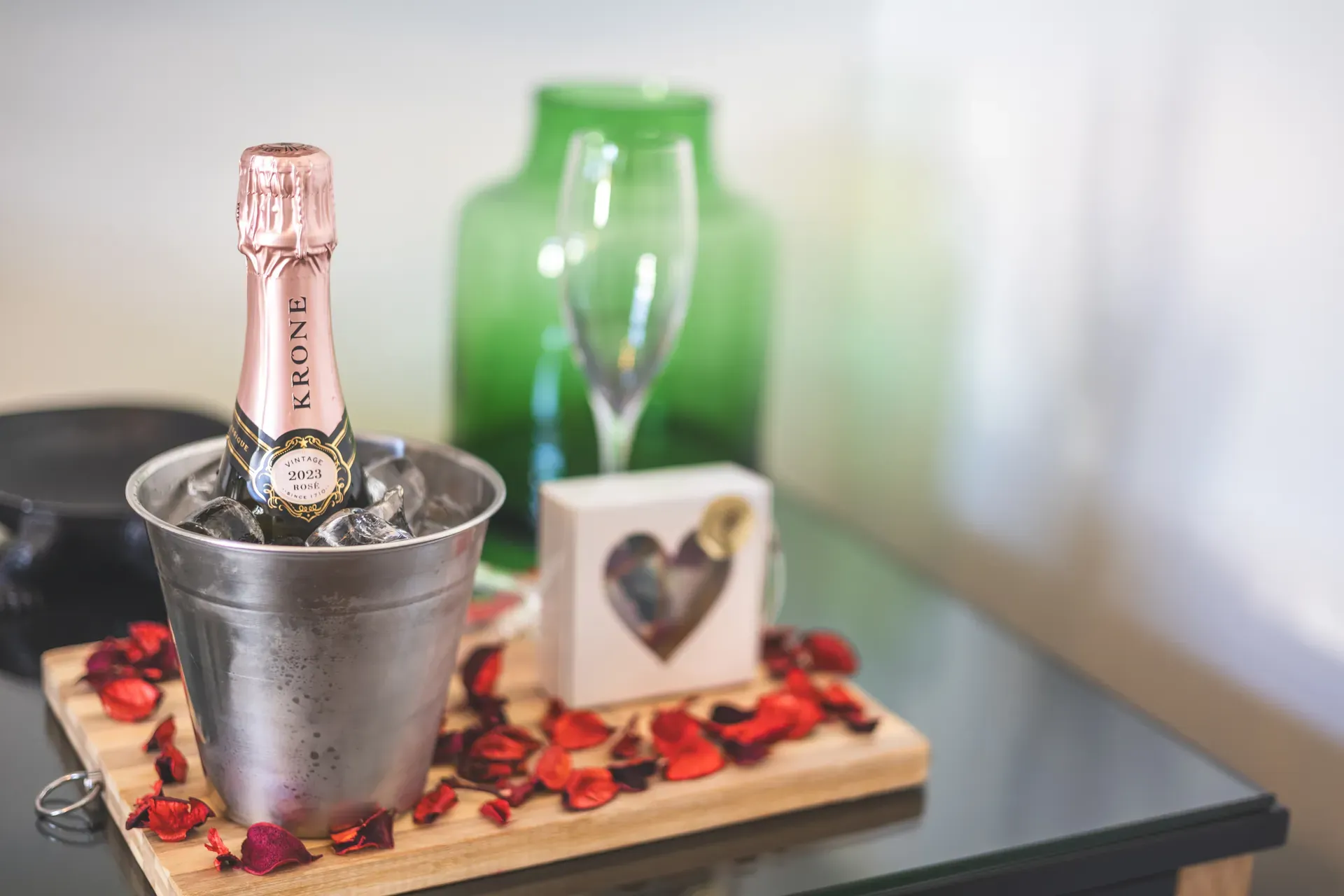 Honeymoon and anniversary treat featuring champagne glasses, a green bottle, strawberries, and a heart-shaped sign on a tray