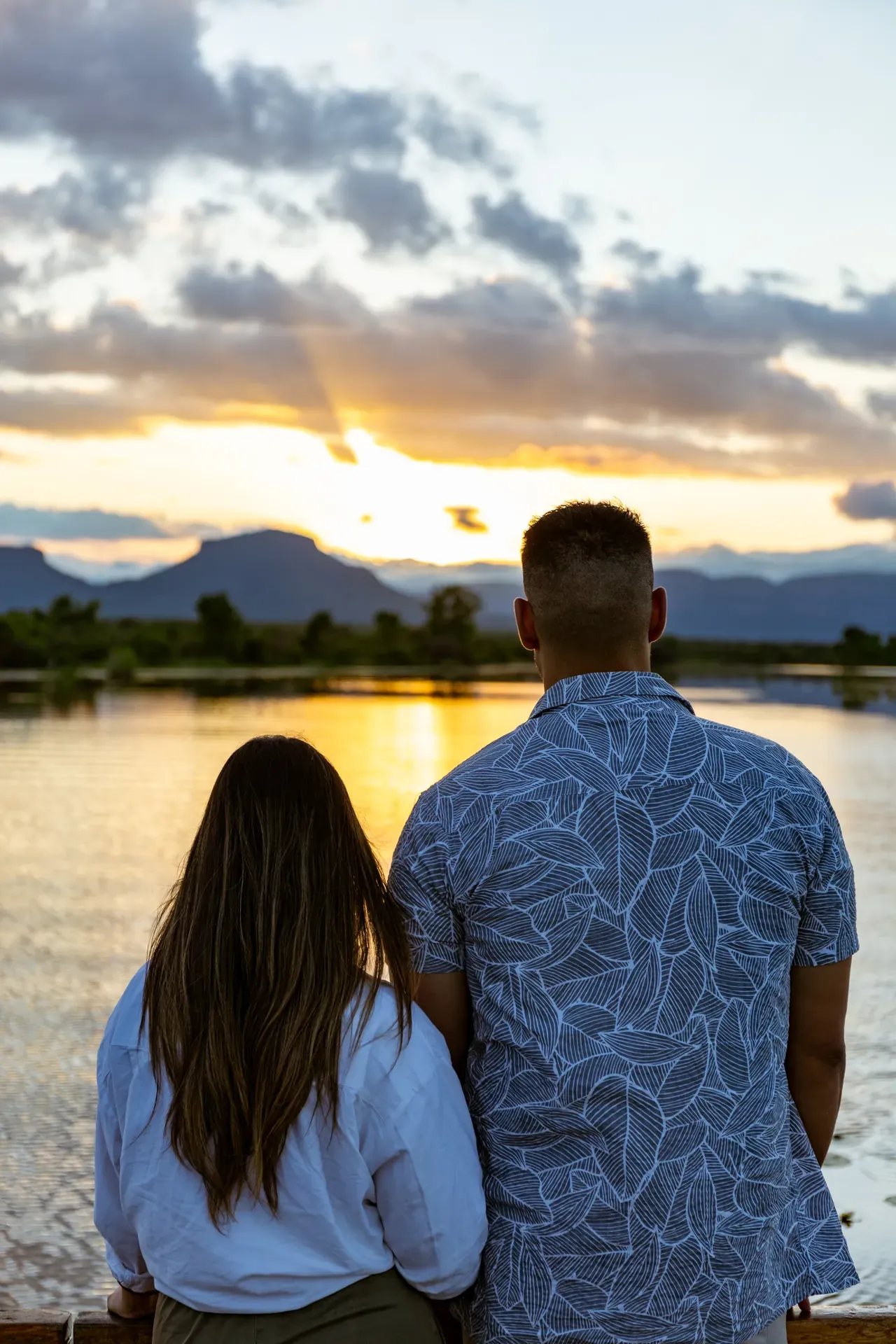 Couple enjoying a sunset experience by the water, sitting on the shore and gazing at the colorful sky over a calm lake