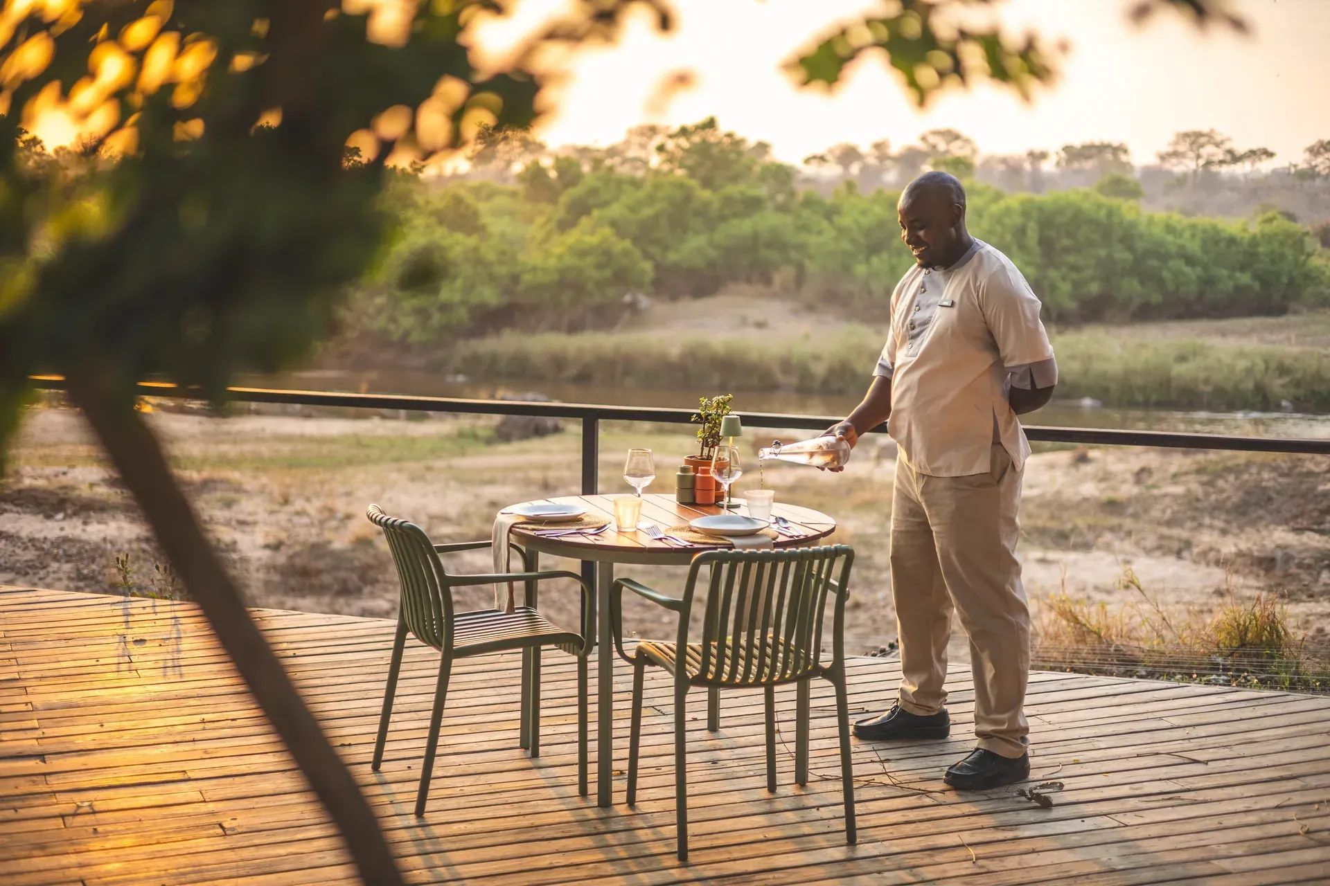Trained safari staff member preparing an outdoor dining setup in the bush with tables and chairs
