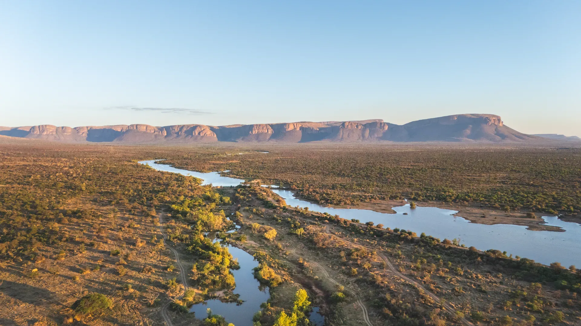 Aerial drone view of a winding river flowing through a rocky landscape with hills in the background