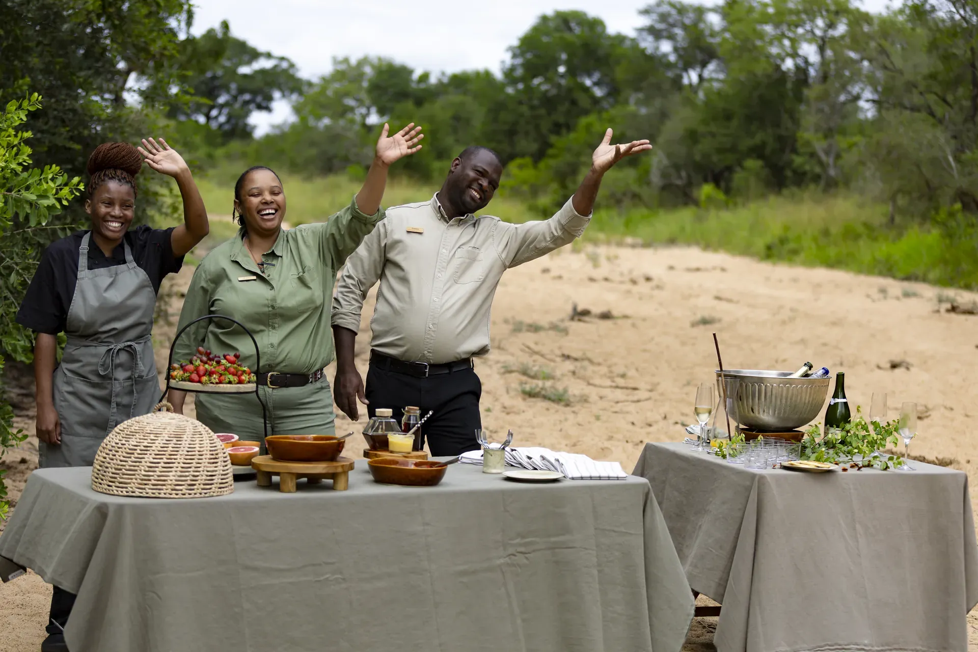 Chef preparing a canape table outdoors with dishes and drinks at Monwana canape stop near a sandy area and greenery
