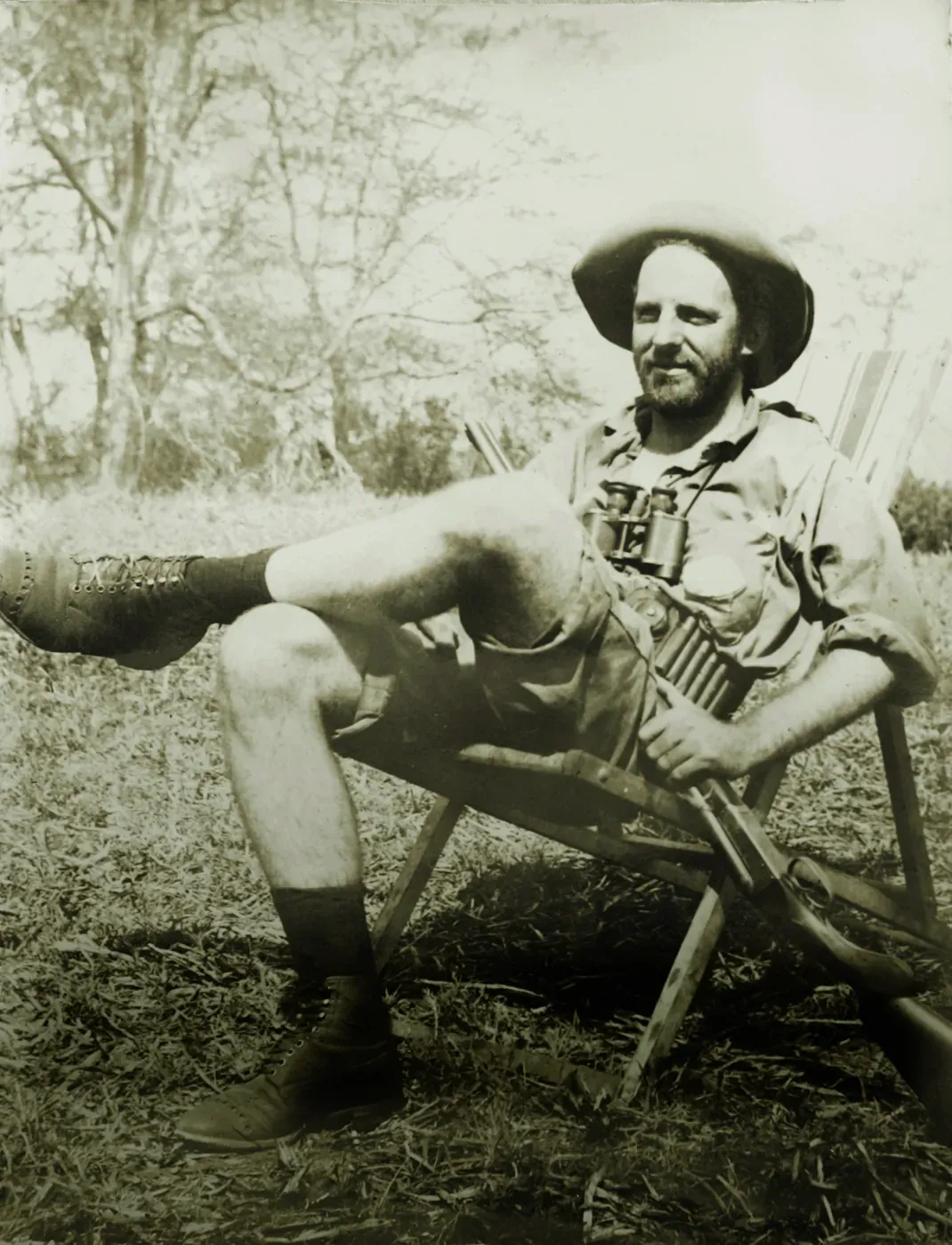 Black and white portrait of a man sitting on a bench outdoors wearing a hat and holding a cane