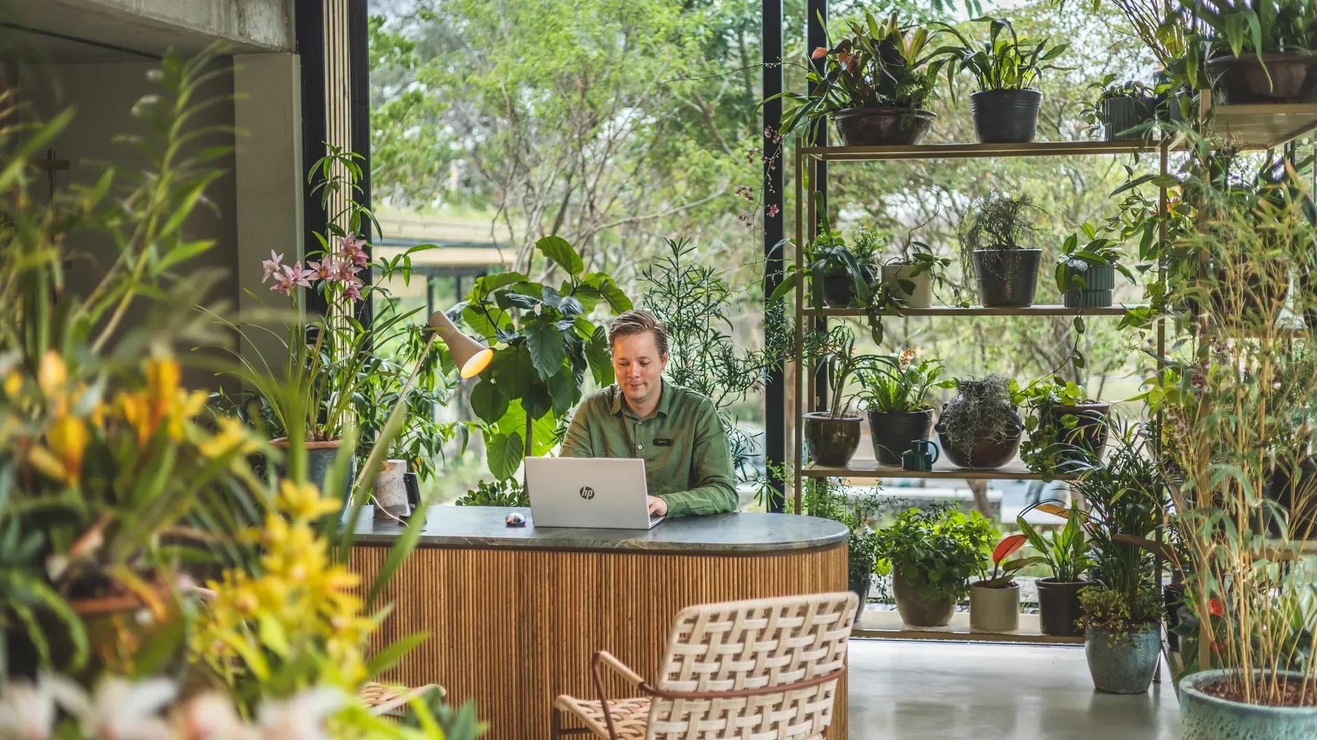 Orchid House reception area featuring wicker chairs, a wooden table, and lush greenery with large windows