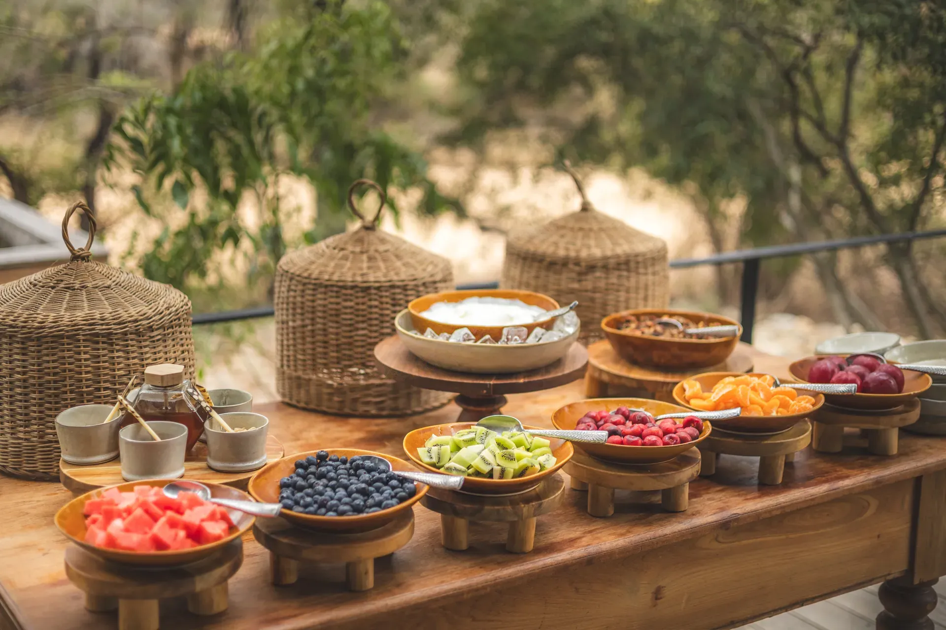 Breakfast harvest table on the deck at Monwana Lodge, piled with fresh fruit, with the African bush in the background."