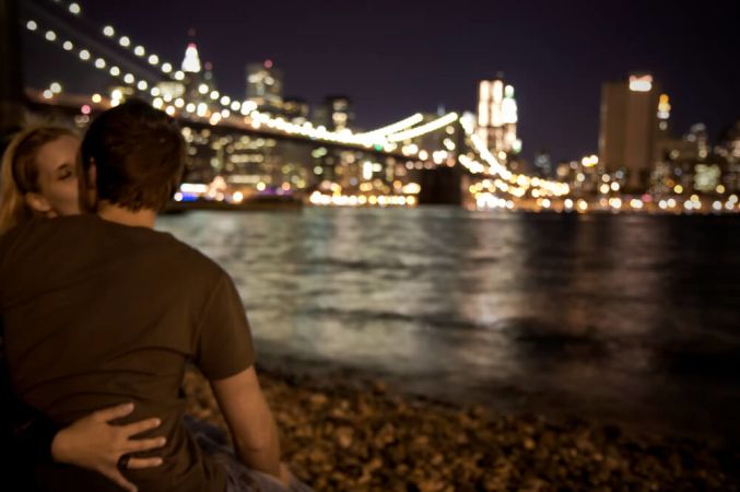 Picture shows a romantic couple looking out over New York City at night.