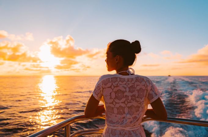 Picture shows a woman enjoying the beautiful views from a cruise ship as the sun sets over the ocean. 