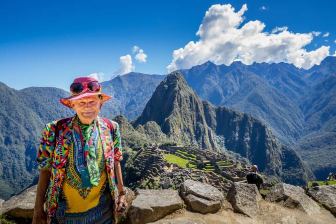 Picture shows an older man posing at Machu Picchu, in Peru. Behind him the Andes mountains rise into the blue sky.