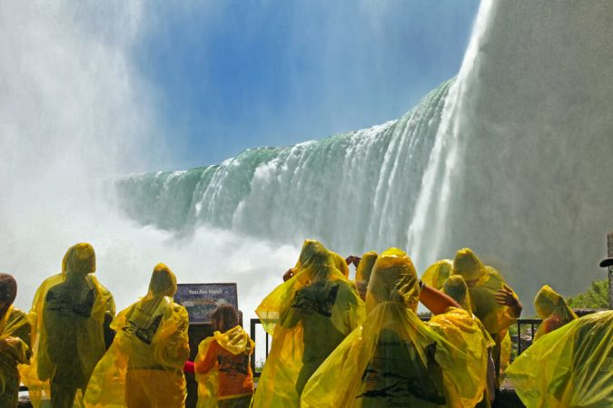 Picture shows a group of tourists in waterproof covers at the amazing Niagara falls.