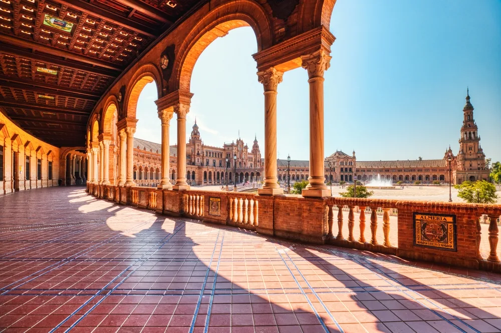 View of Plaza de España in Seville, Spain, with sunlit arches and tiled walkway